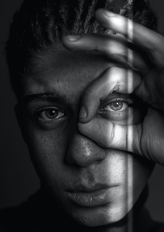 A black and white image of a guy highliting his right eye with his hand. Tear Trough filler. Aesthetic Treatments at Teresa Tarmey