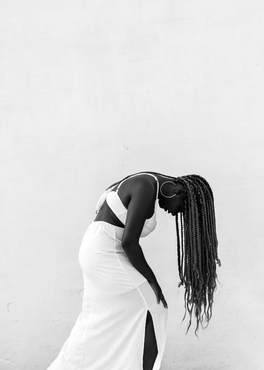 Black woman with long braided hair in white cutout dress flipping her hair. Cosmelan Peel Treatment at Teresa Tarmey 